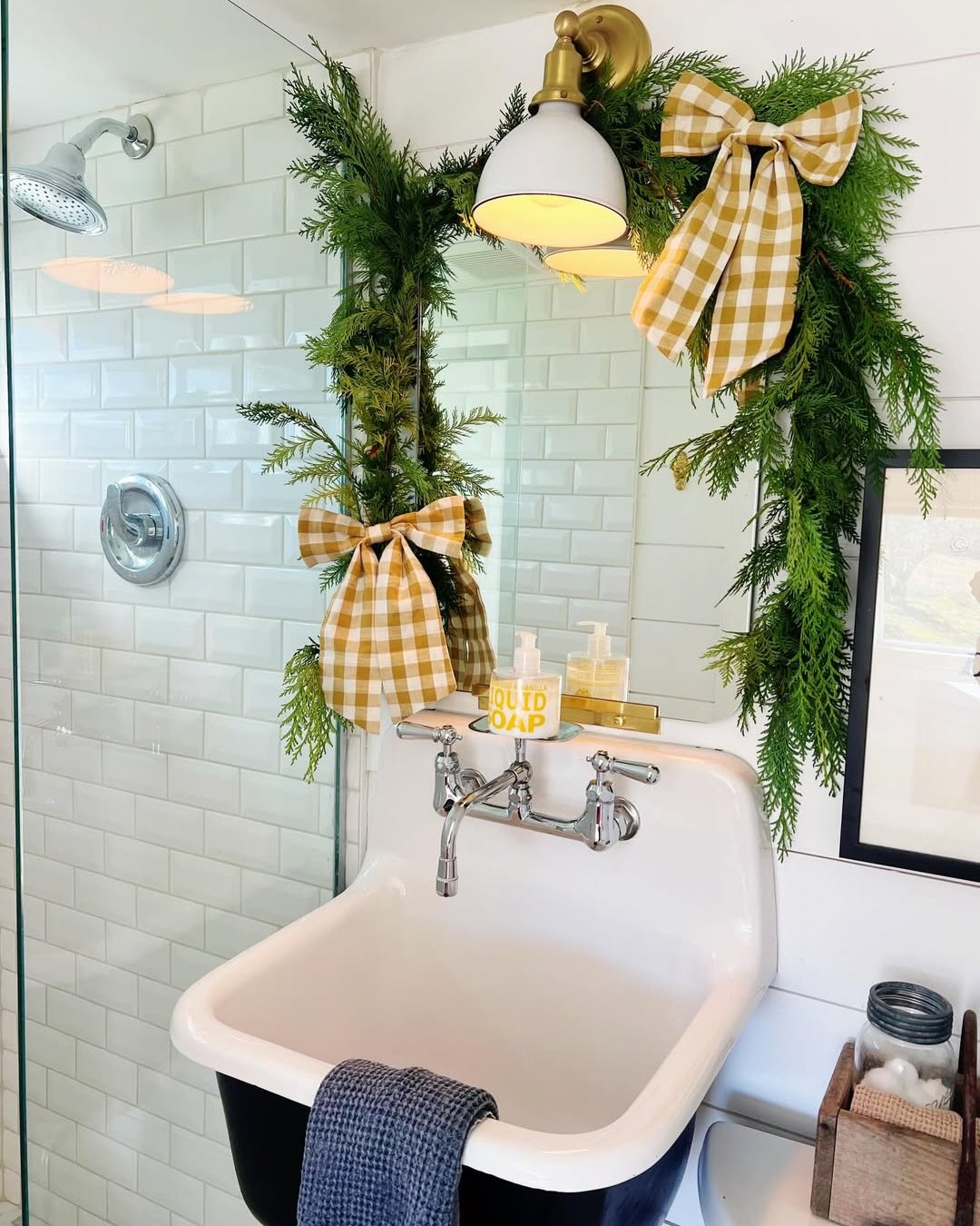 Cedar garland and gingham bows frame a vintage bathroom mirror for cheerful holiday styling