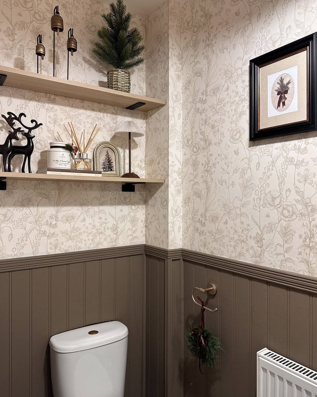 Alt text: Cozy holiday bathroom with evergreen tree, wreath, bells, reindeer, and floral wallpaper