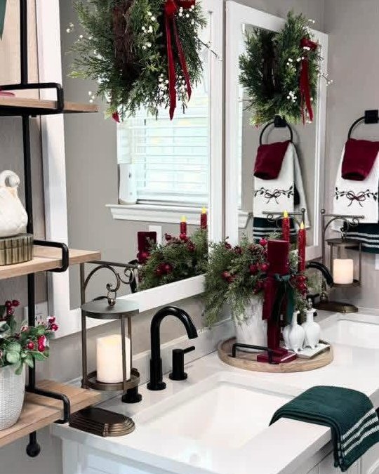 Christmas-inspired bathroom vanity with evergreen garlands, red ribbons, candles, and festive hand towels