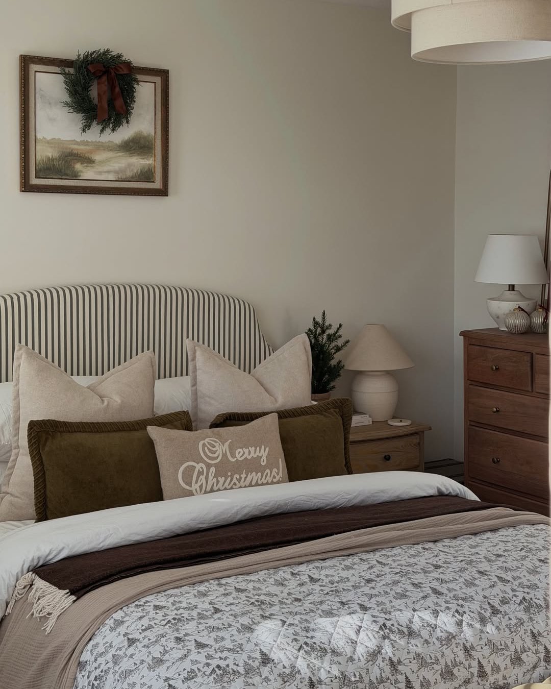 Soft neutral Christmas bedroom with an evergreen wreath, layered pillows, and cozy seasonal bedding