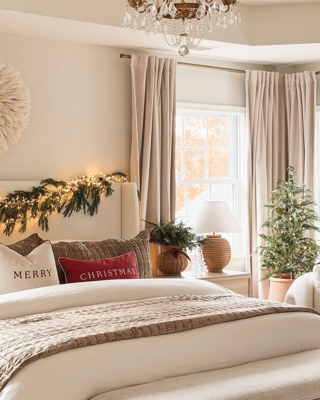 Warm Christmas bedroom with glowing garland, neutral bedding, red pillows, and a softly lit tree
