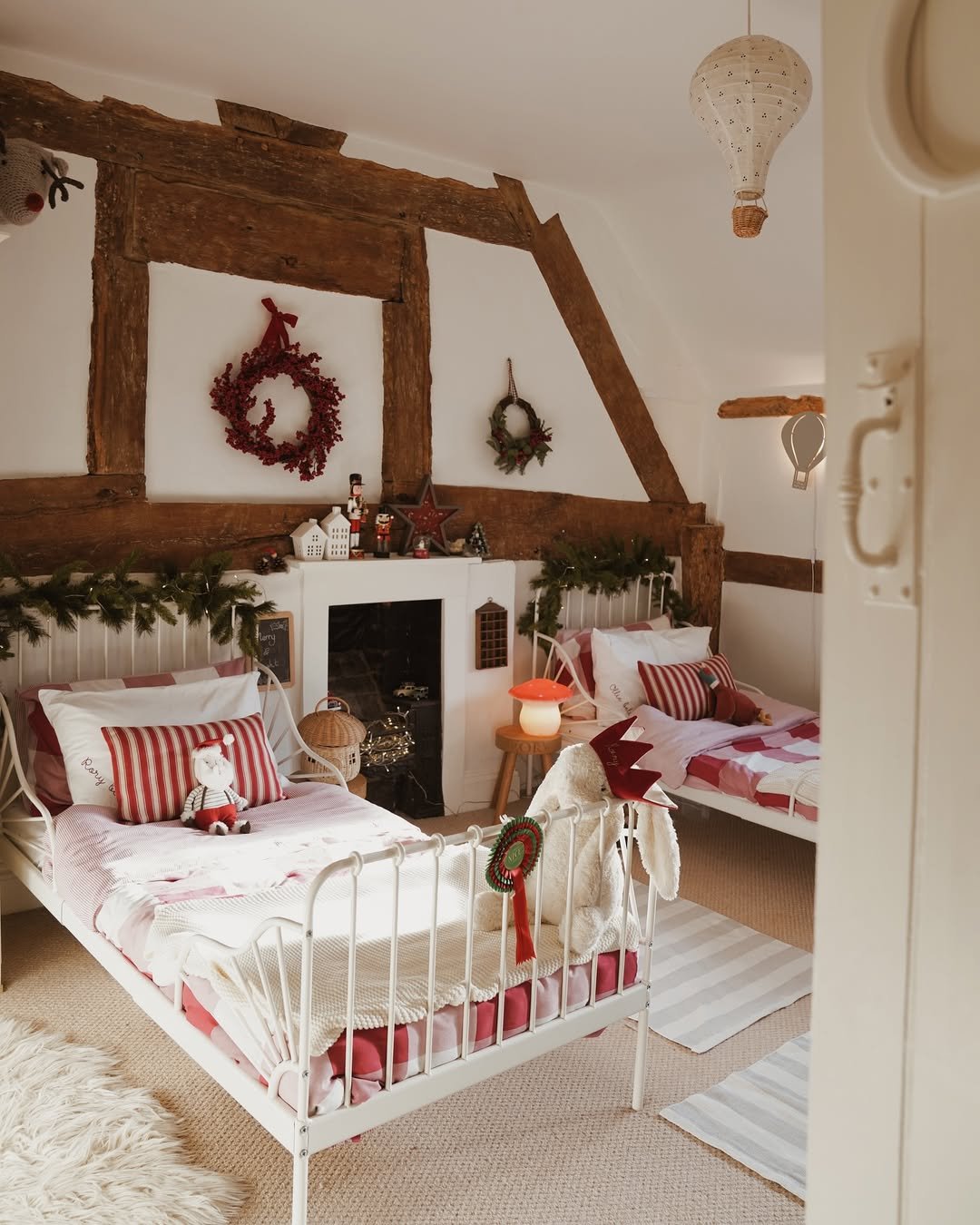 Festive farmhouse bedroom with evergreen garlands, striped bedding, wreaths, and rustic timber beams