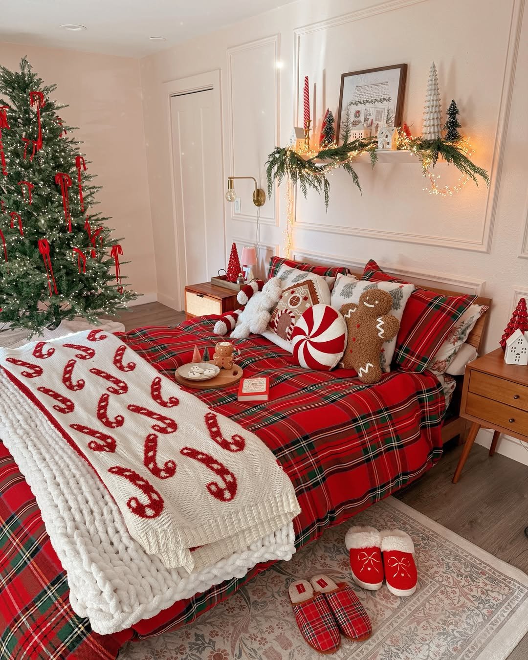 Red plaid holiday bedroom with candy cane blanket, glowing Christmas tree, garland, gingerbread pillows, and festive slippers