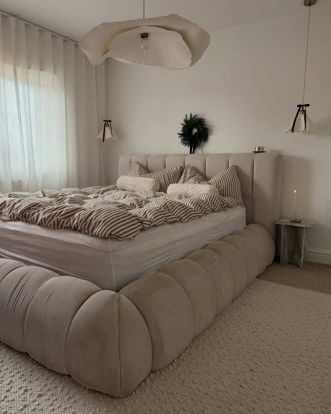 Neutral Christmas bedroom with striped bedding, upholstered bed, greenery wreath, and soft candlelight