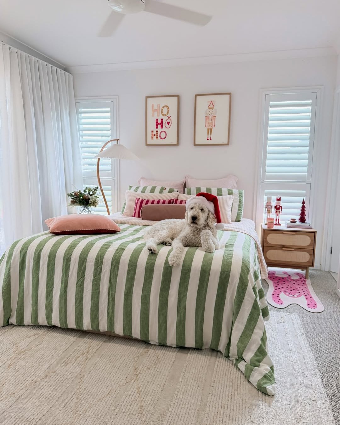 Christmas bedroom with green striped bedding, festive wall art, nutcrackers, and a dog wearing a Santa hat
