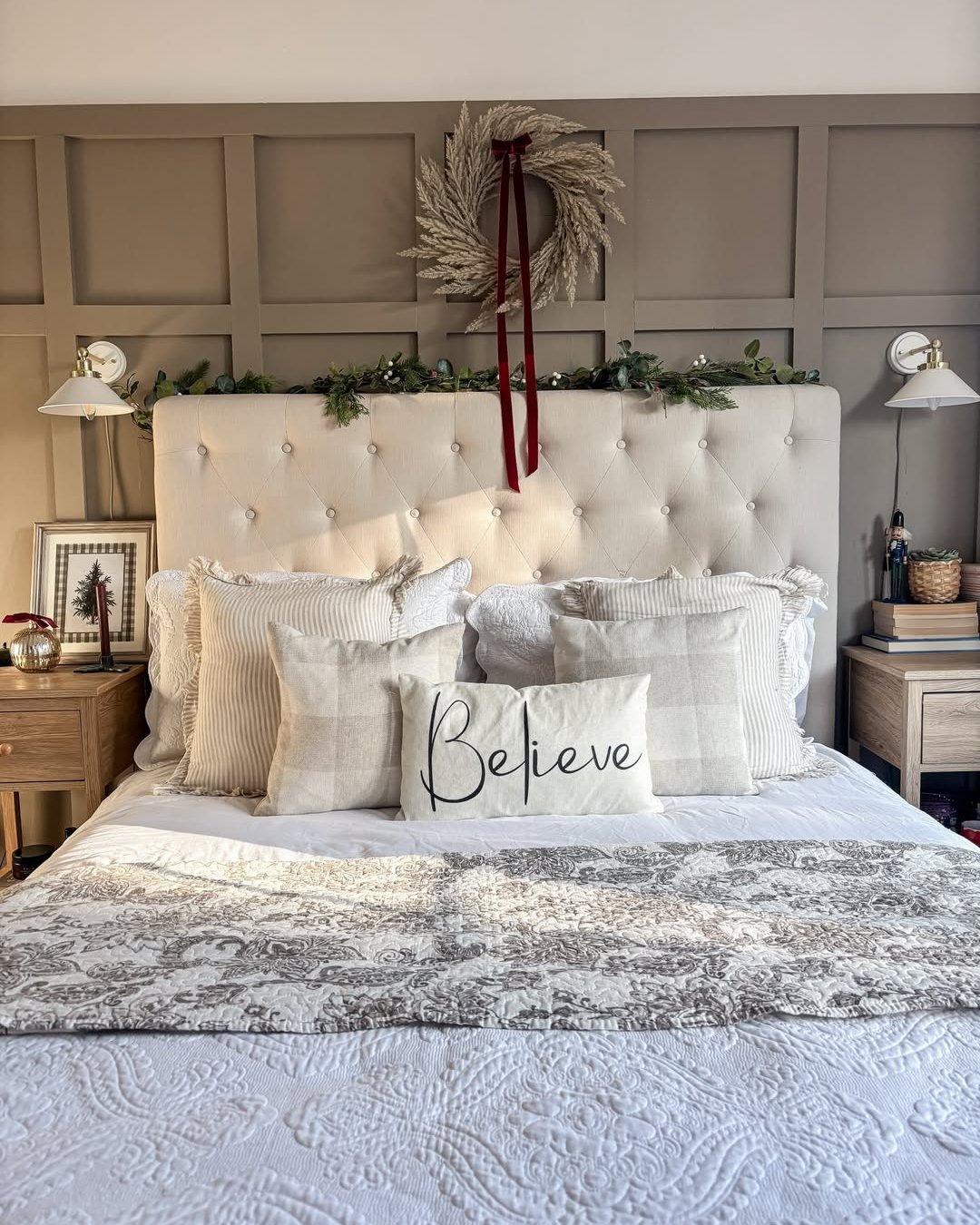 Frosted wreath, greenery, burgundy ribbon, and layered bedding create a serene holiday bedroom