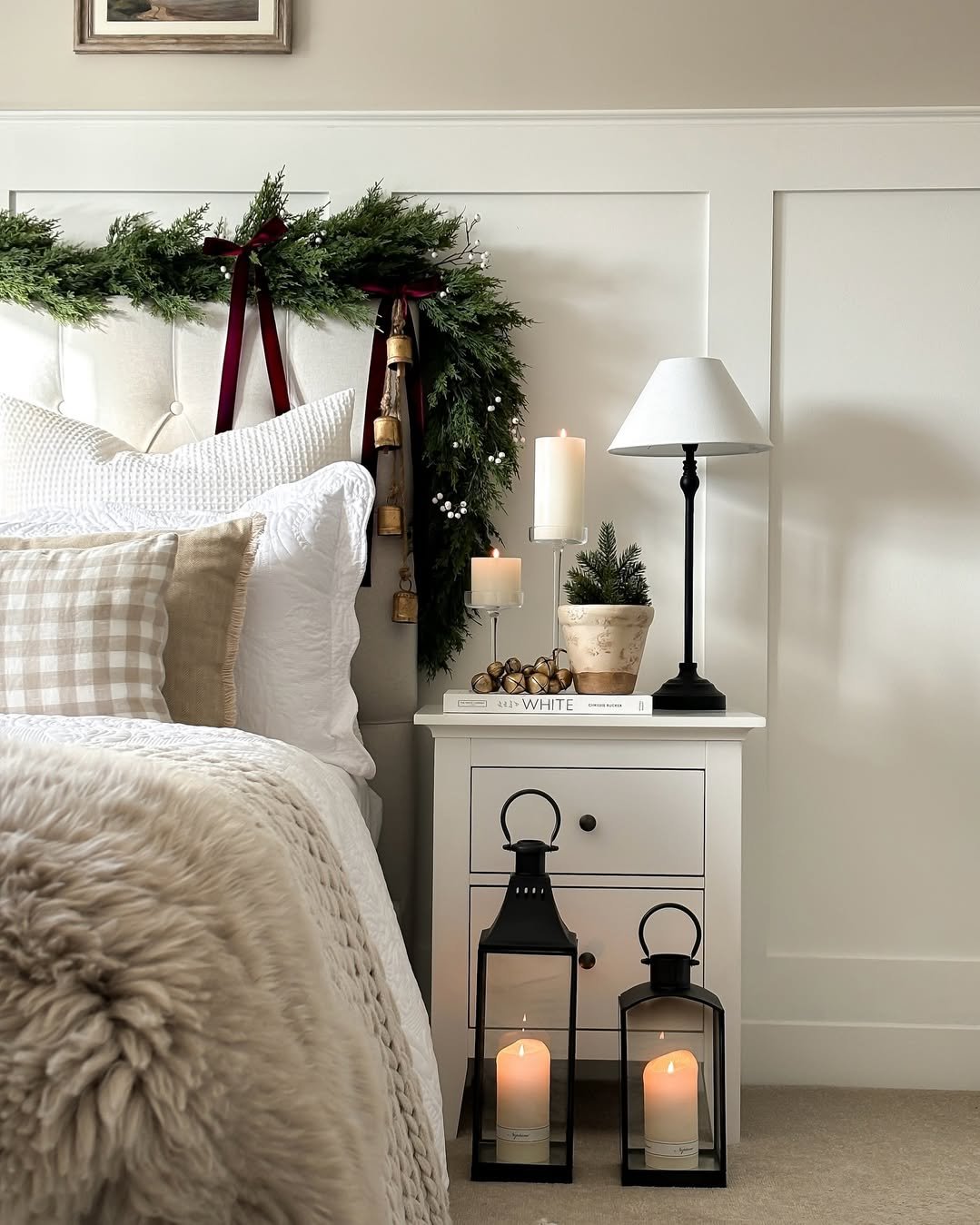 Evergreen garland, bells, candles, and cozy neutral bedding create festive holiday bedroom styling