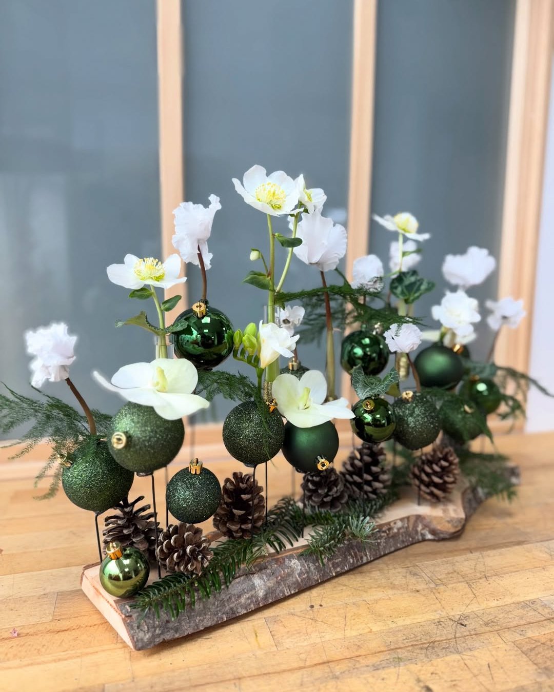 White flowers and green ornaments arranged with pinecones and evergreen branches in a festive centerpiece