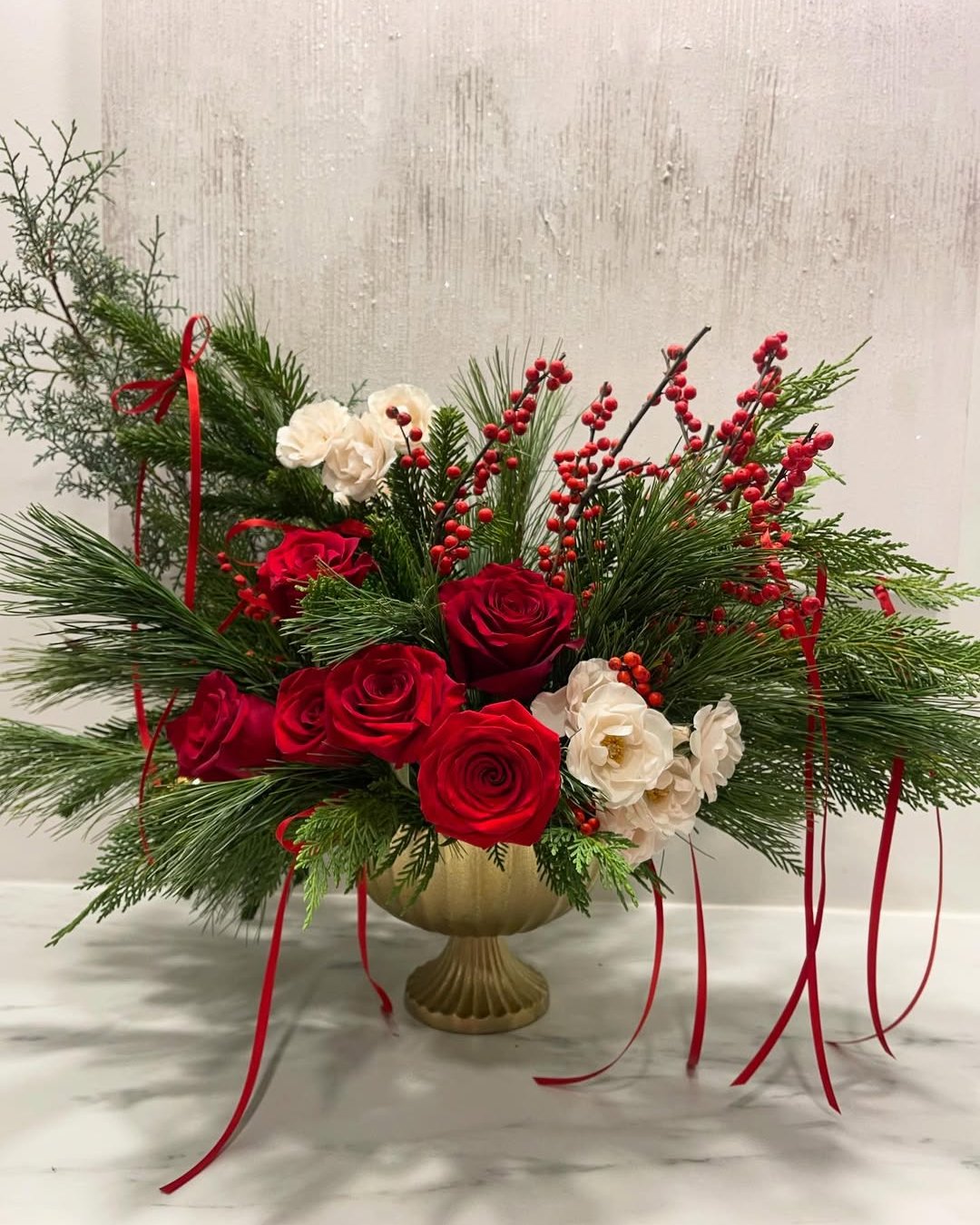 Red roses, white blooms, evergreen branches, berries, and trailing ribbons in a festive holiday centerpiece
