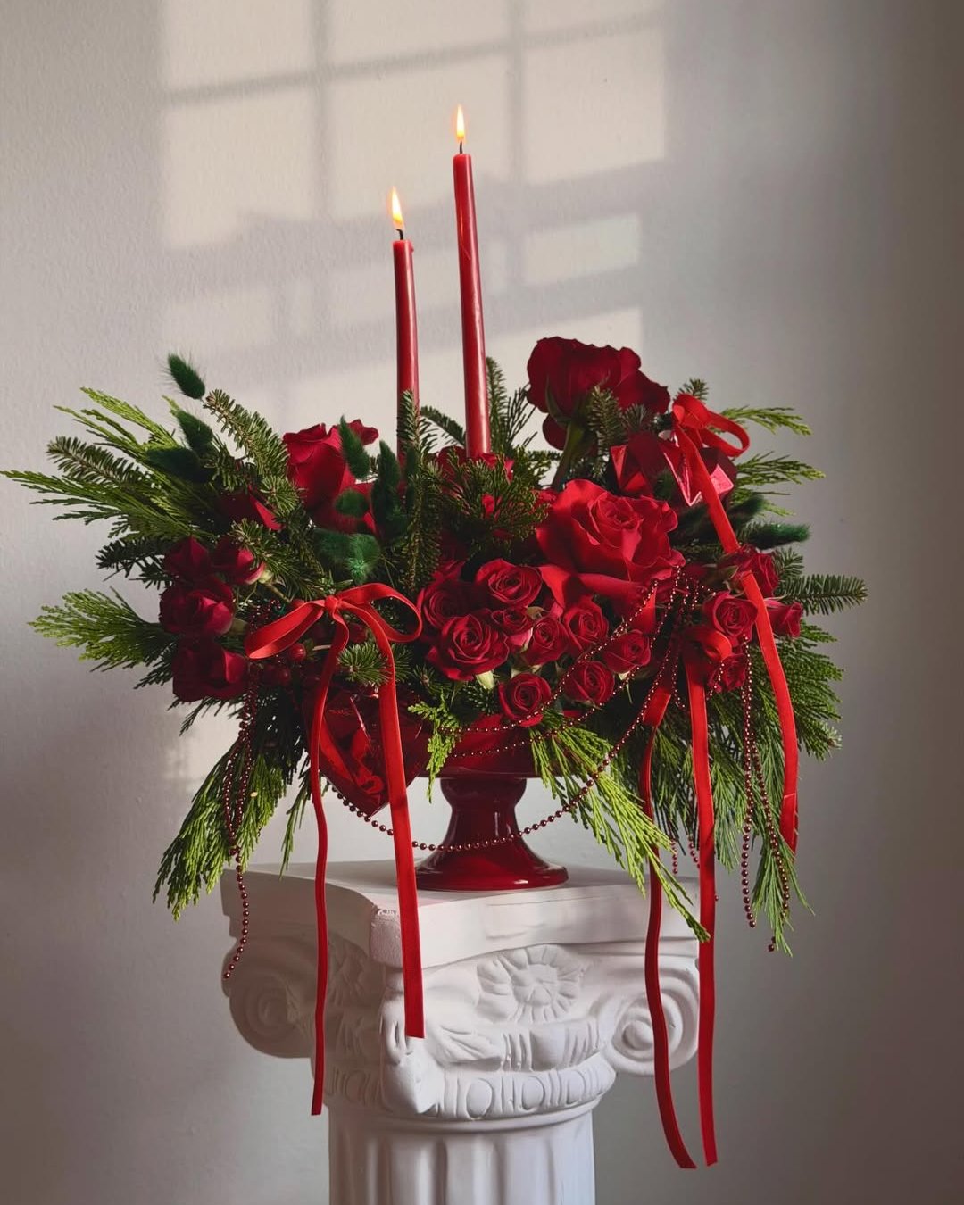 christmas floral arrangements with red roses, evergreen branches, taper candles, ribbons, and bead garlands