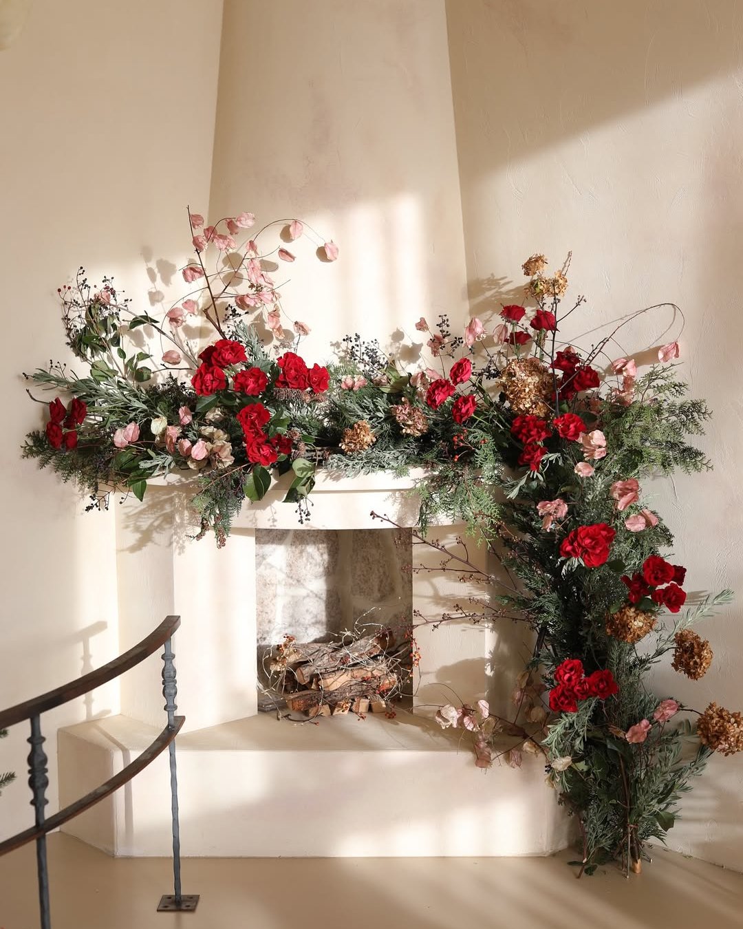 Red roses and pink blooms woven through an evergreen fireplace garland