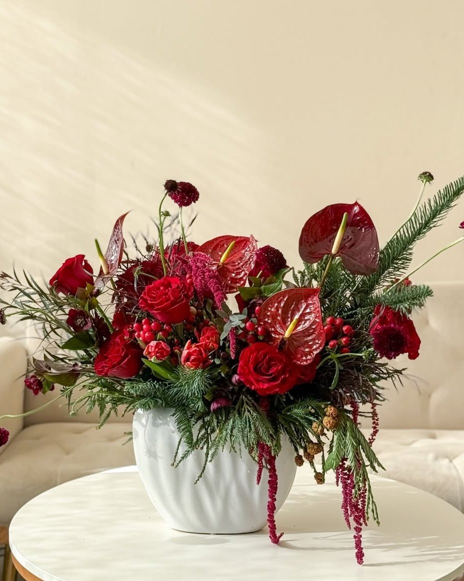 Crimson holiday centerpiece with roses, anthuriums, berries, and evergreen branches in a white vase