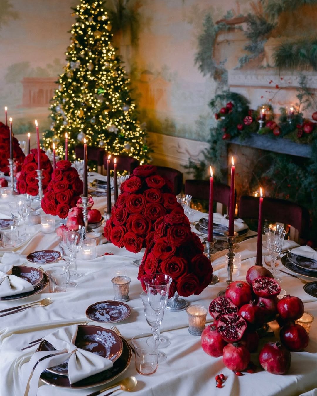 Red rose holiday table centerpiece with candles, pomegranates, evergreen branches, and glowing Christmas decor