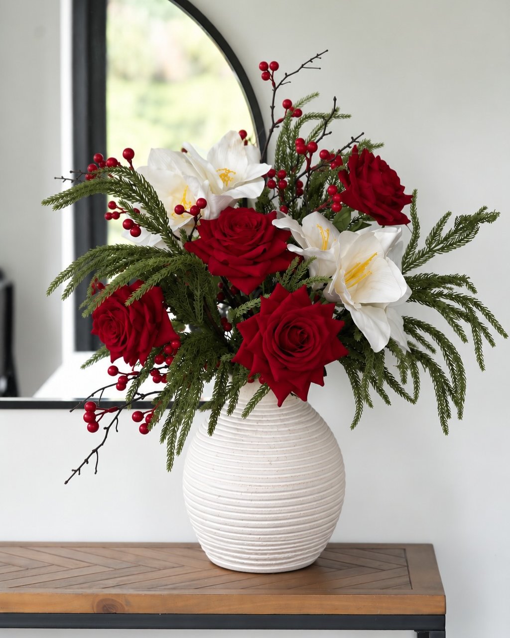 Red roses, white lilies, evergreen branches, and berries arranged in a festive holiday vase