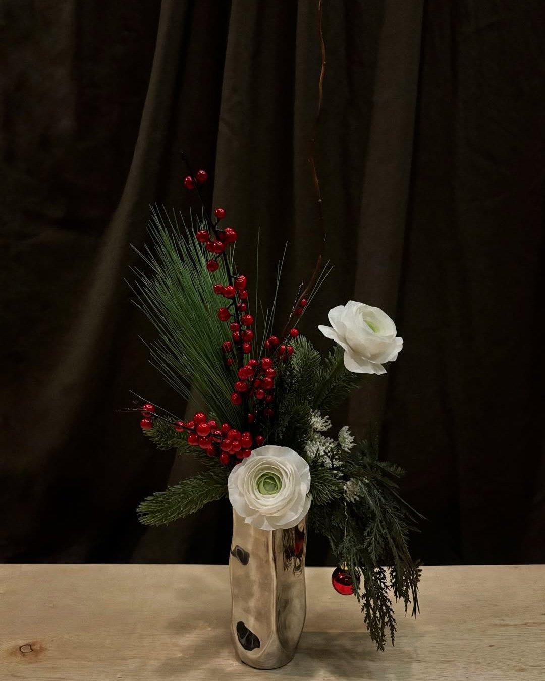 White ranunculus, red berries, and evergreen Christmas centerpiece in a reflective silver vase