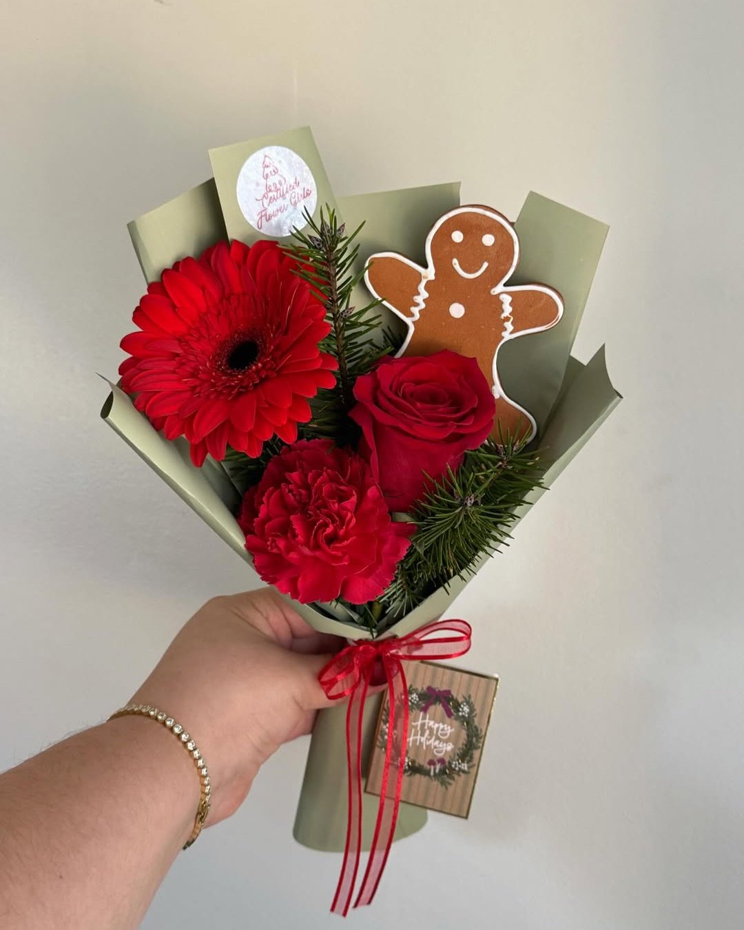 christmas floral arrangements with red flowers, evergreen sprigs, gingerbread cookie, sage wrapping, and red ribbon