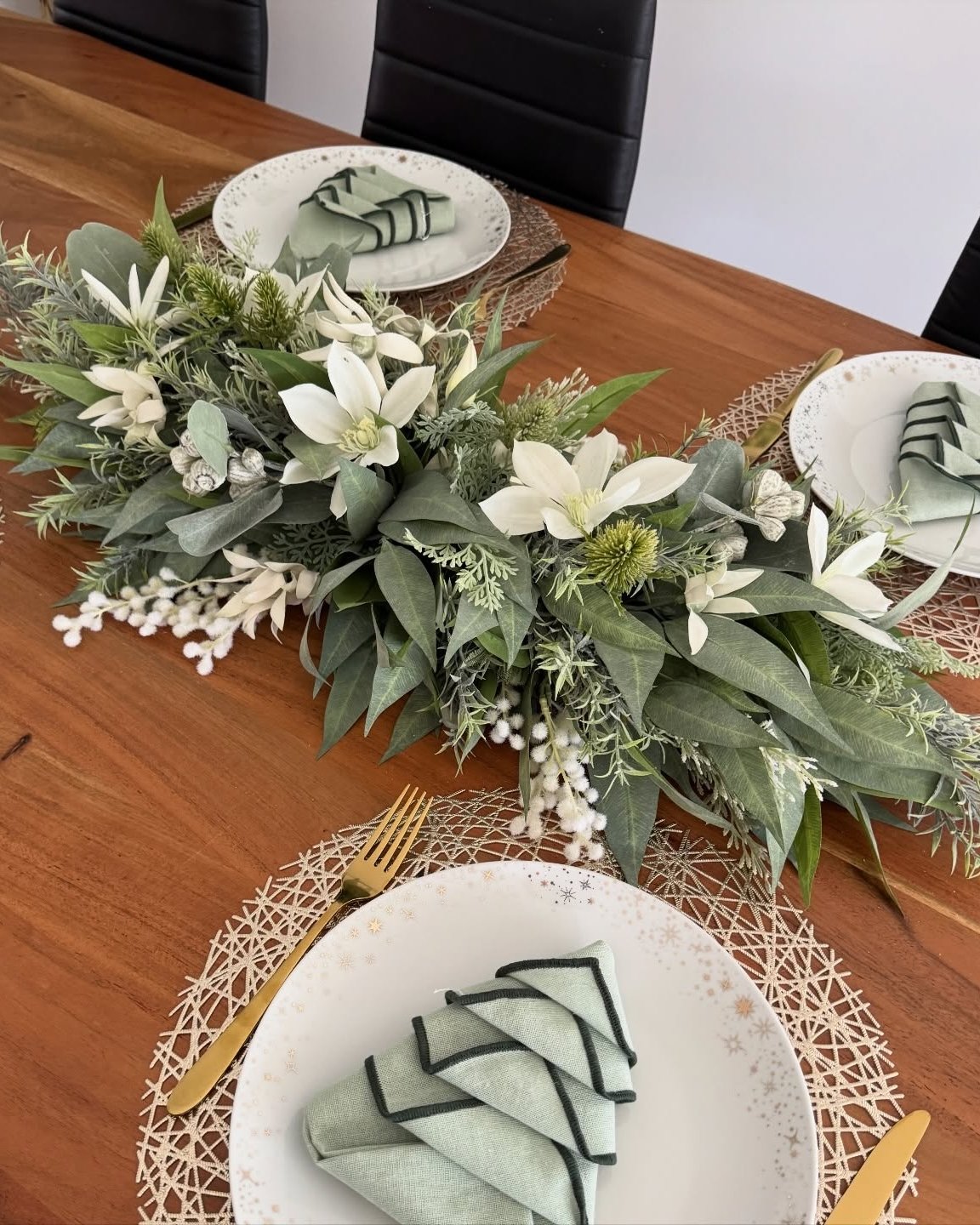 Soft evergreen holiday table runner with white blooms, frosted foliage, and sage place settings