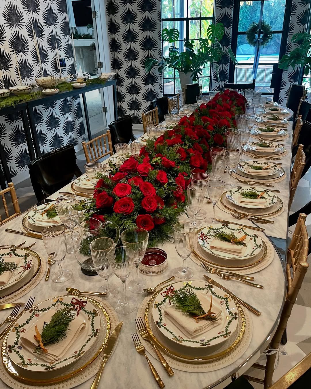 Red roses and evergreen centerpiece surrounded by festive place settings and gold-rimmed china