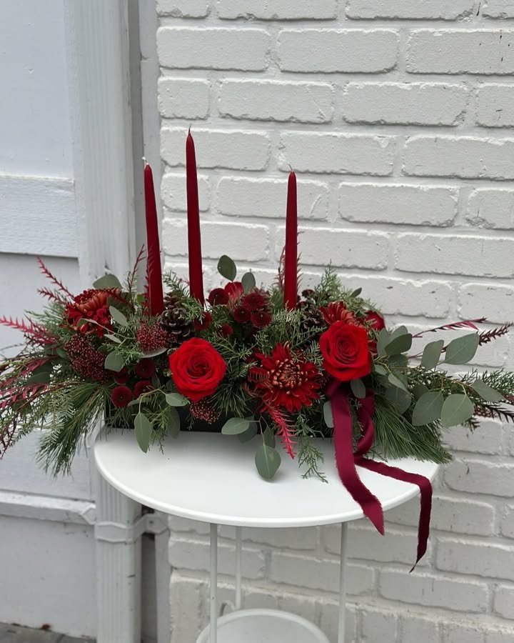 Crimson holiday centerpiece with roses, candles, evergreen branches, eucalyptus, berries, and pinecones