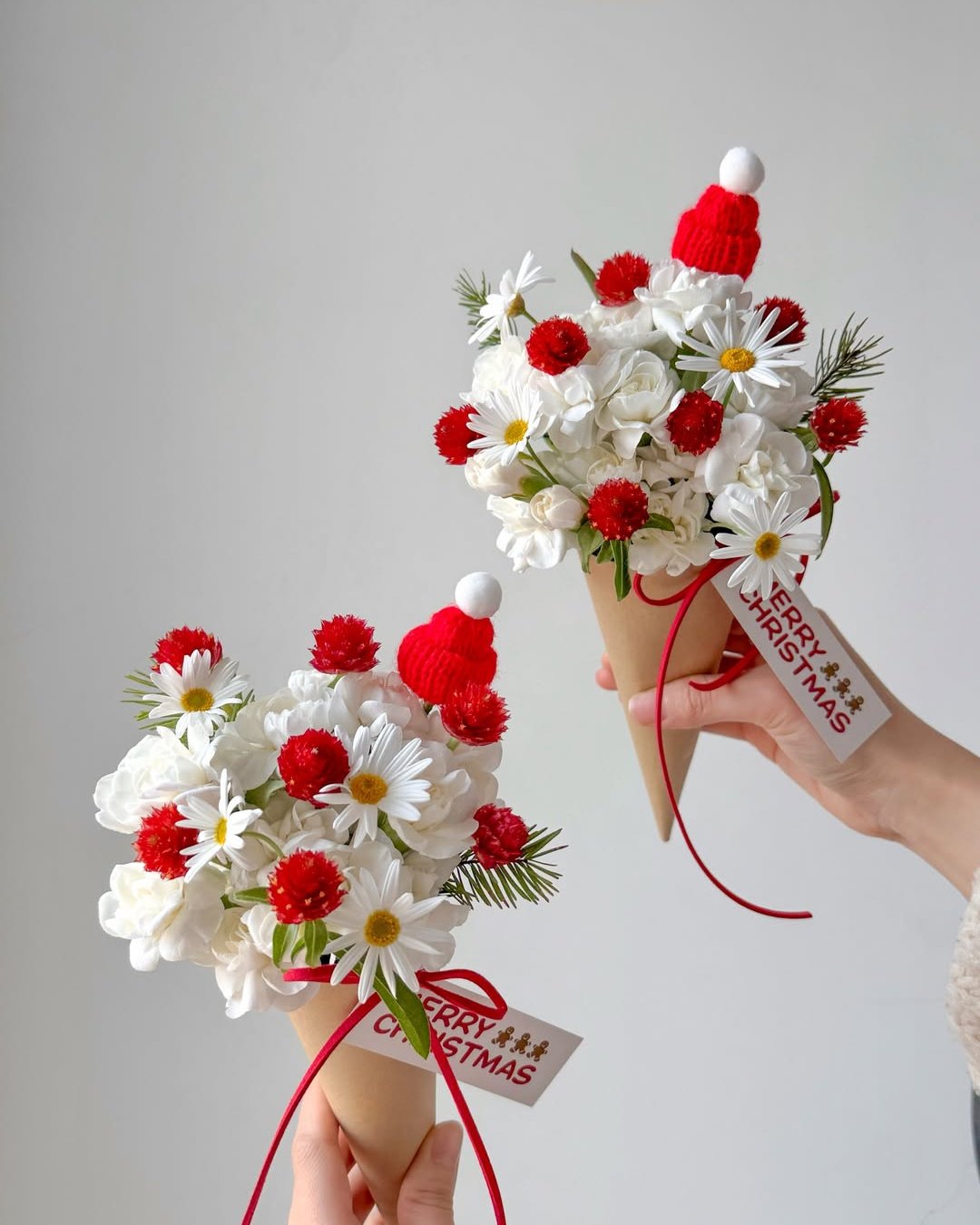 White and red holiday bouquets with daisies, roses, greenery, and tiny Santa hats