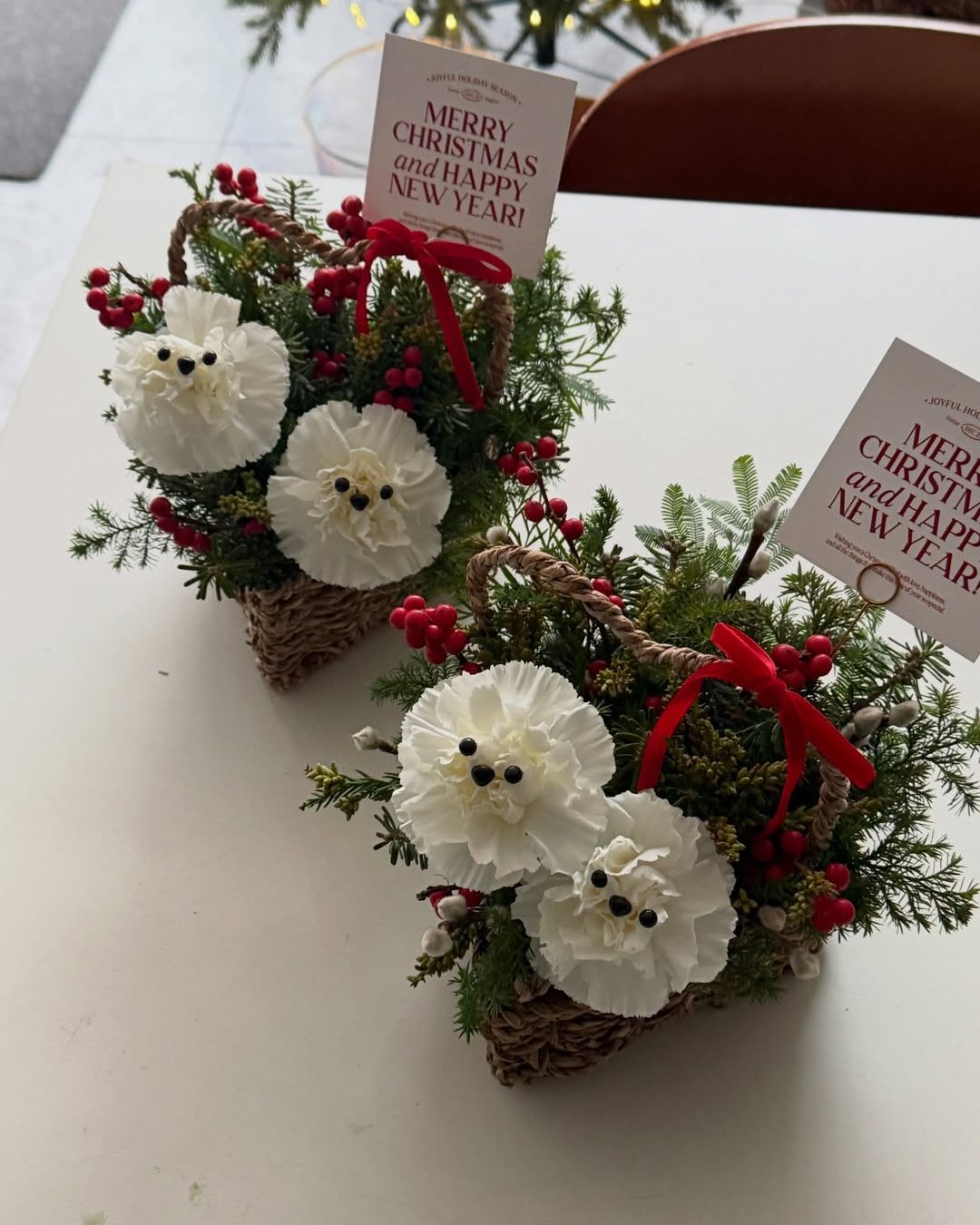 White flower holiday baskets with evergreen sprigs, red berries, bows, and greeting cards