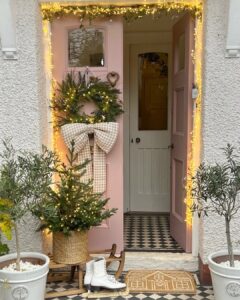 Christmas front door decor ideas with a glowing evergreen wreath, gingham bow, and potted tree
