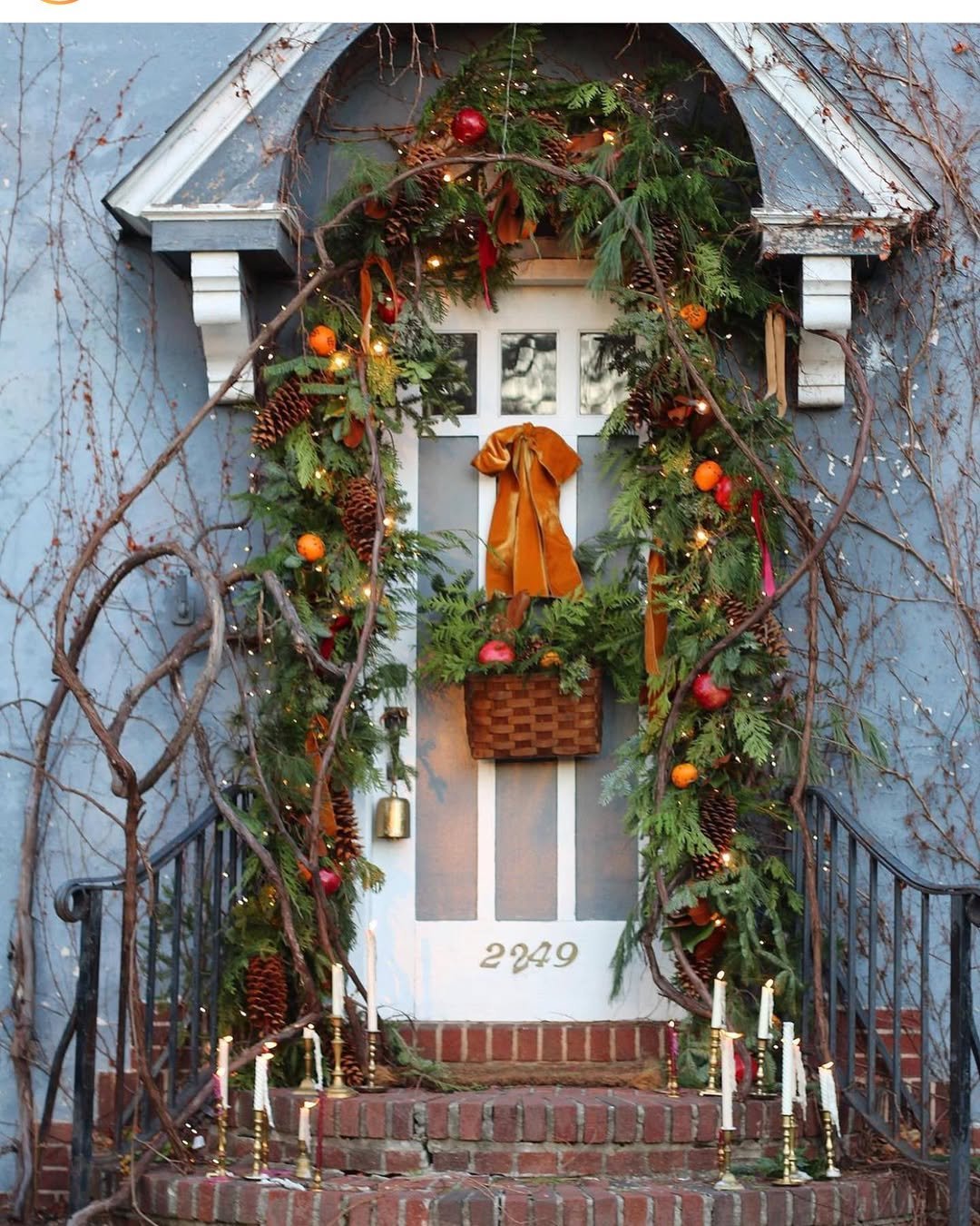 Evergreen garland with pinecones, fruit, twinkle lights, and velvet ribbon surrounding a festive entryway