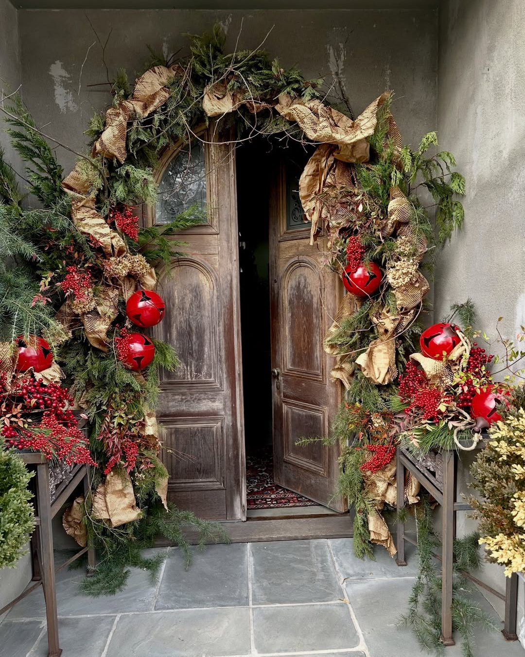Red ornaments and burlap ribbon frame a rustic evergreen holiday doorway