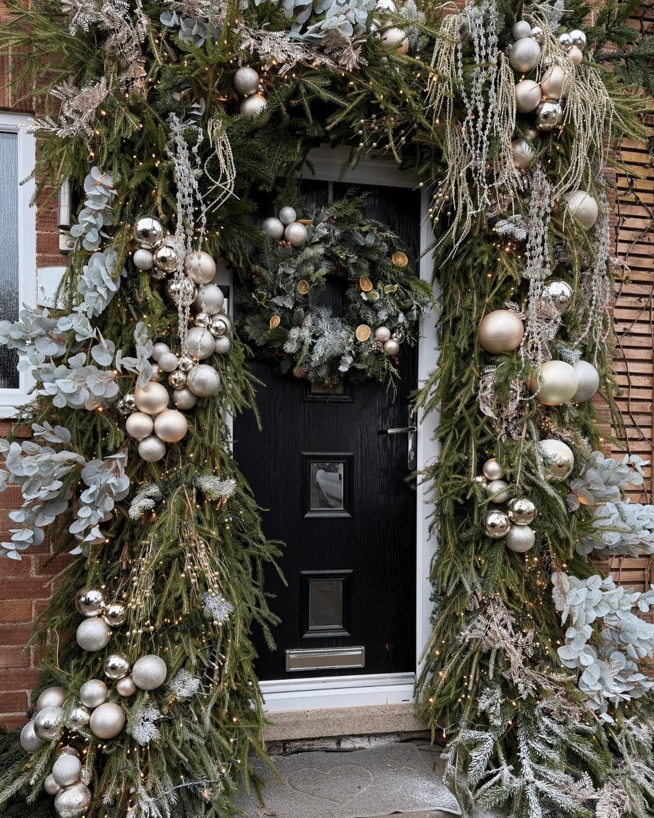 Elegant evergreen doorway with silver ornaments, eucalyptus, lights, and a festive wreath