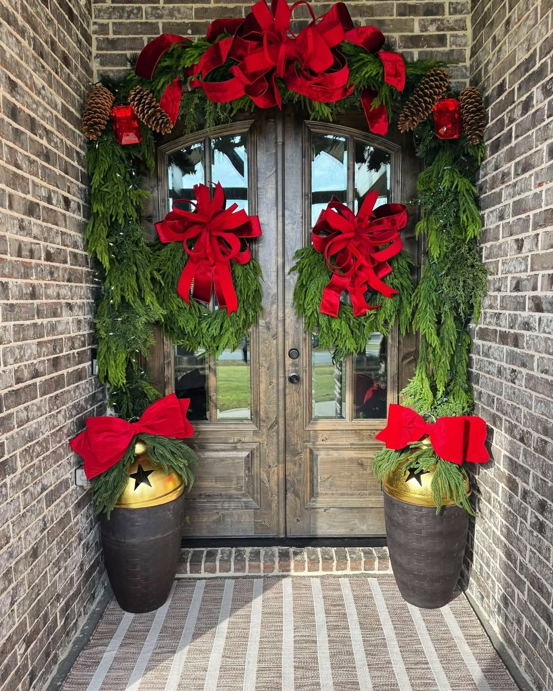 Red bow evergreen garland framing double doors with bell planters