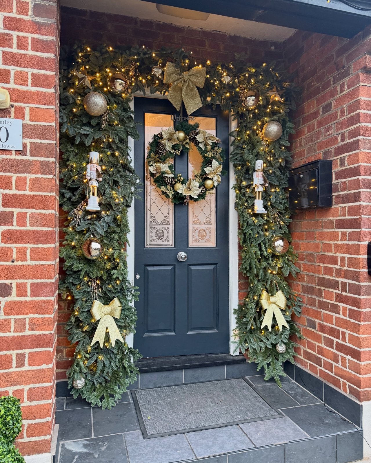 Evergreen garland framing a navy door with glowing lights, gold ornaments, bows, wreath, and nutcrackers