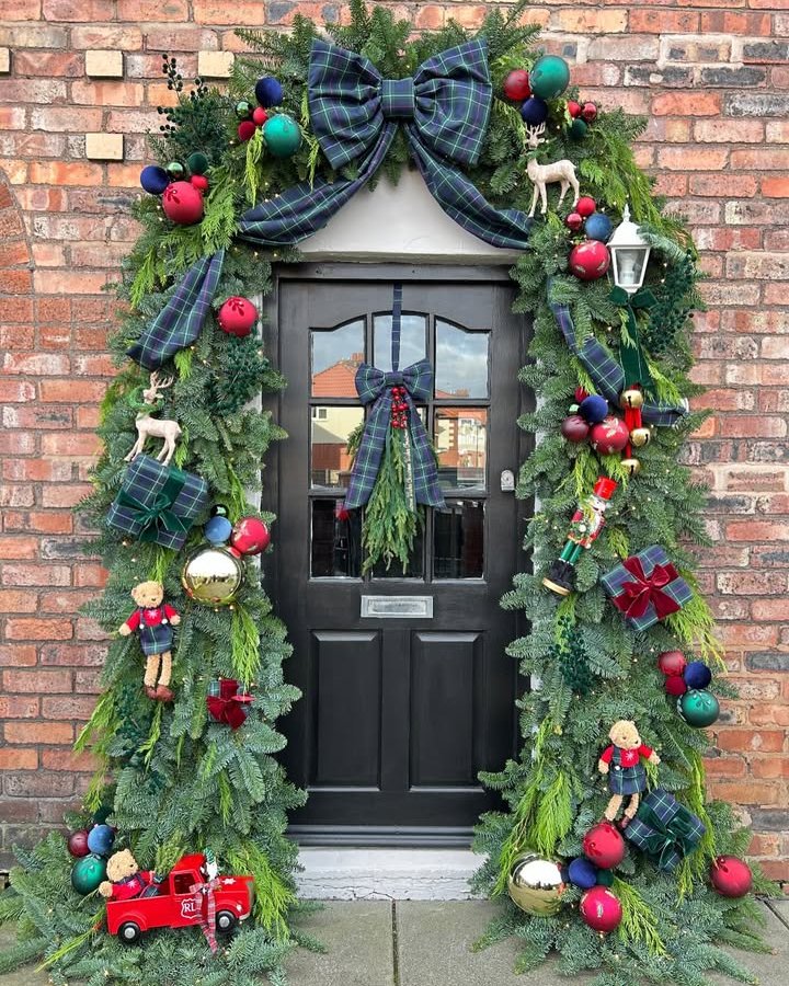 Christmas front door decor ideas featuring tartan bows, evergreen garland, ornaments, reindeer, and toy soldiers