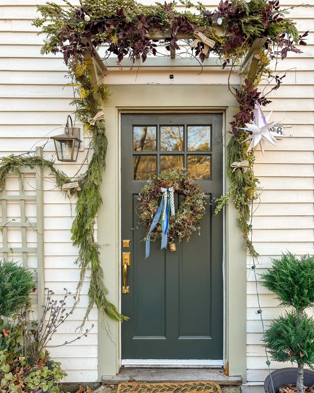 Evergreen garland, wreath, star ornament, and potted trees create a woodland Christmas entry