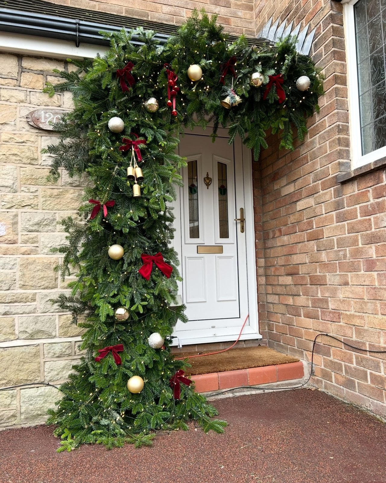 Christmas entryway with cascading evergreen garland, red bows, gold ornaments, bells, and glowing fairy lights