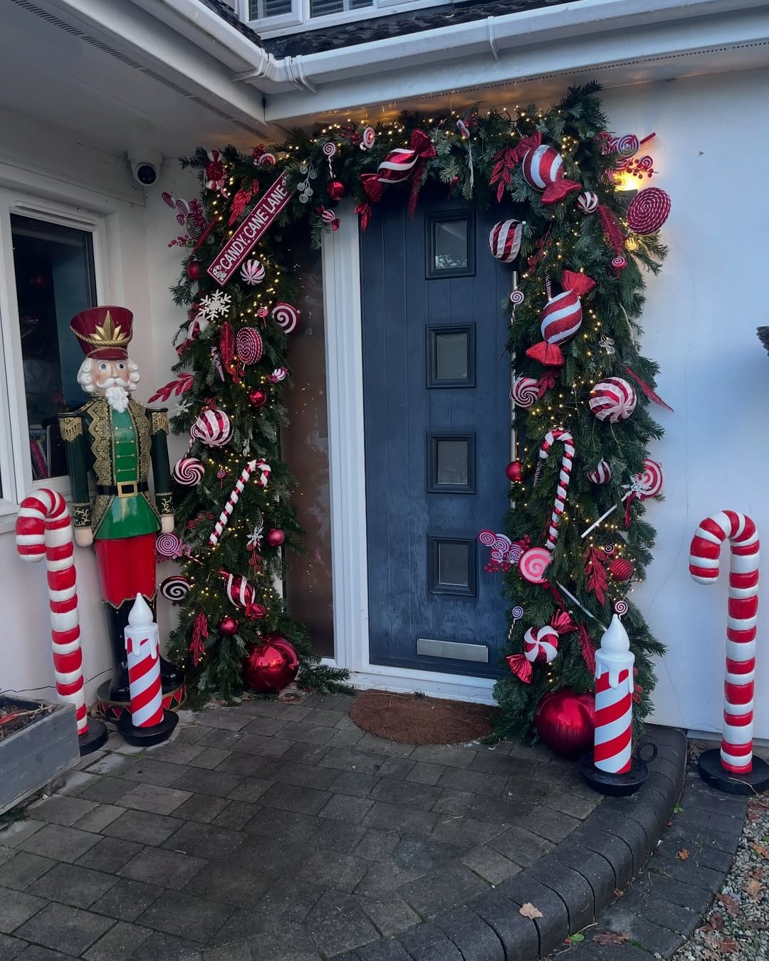 Candy cane Christmas entryway with illuminated evergreen garland and oversized red-and-white ornaments