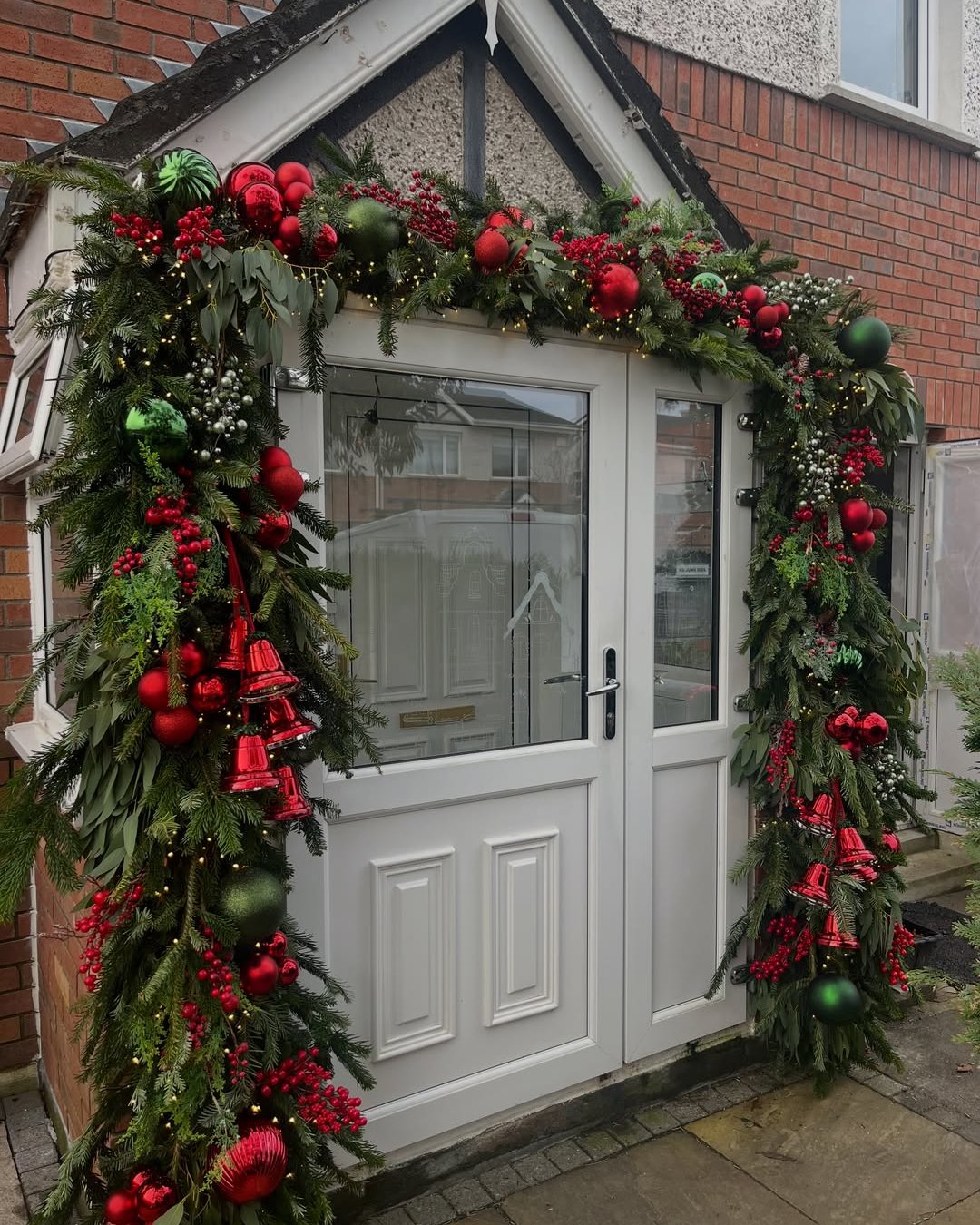 Lush Christmas garland with red baubles and bells framing a white entrance door