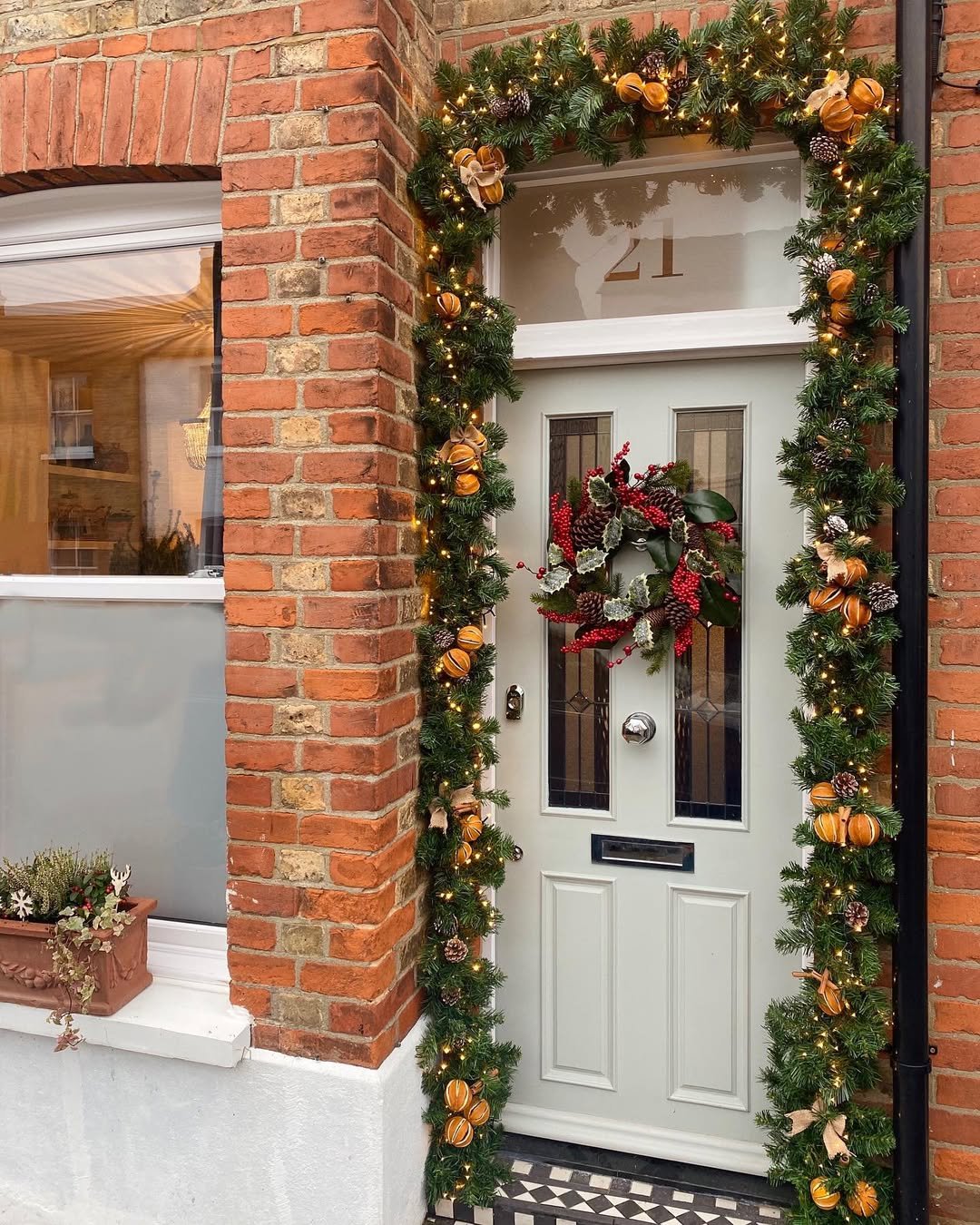 Dried orange and pinecone garland framing a gray door with a berry wreath