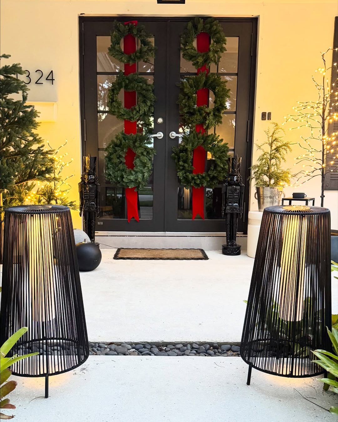 christmas front door decor ideas with paired wreaths, red ribbons, greenery, and glowing porch lights