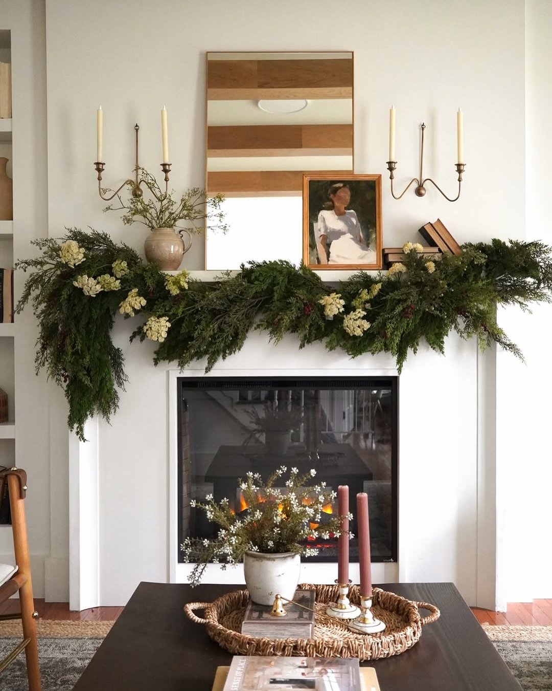 Evergreen floral mantel greenery with blooms, berries, candles, and a warm fireplace
