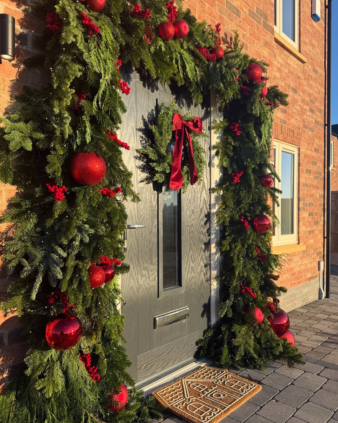 Lush evergreen Christmas doorway garland with red ornaments, berry clusters, and velvet bow
