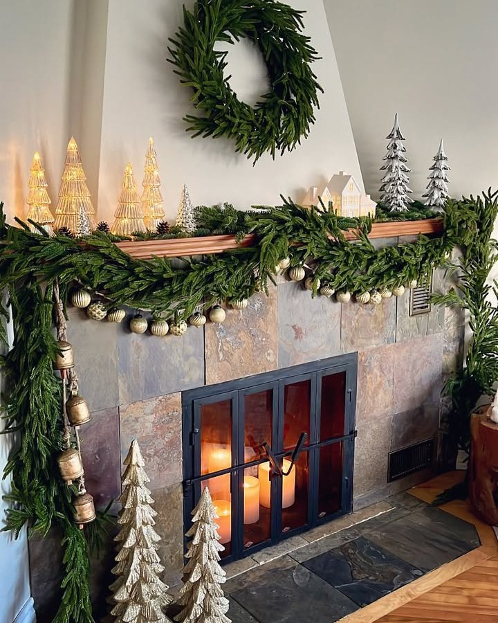 Evergreen fireplace garland with metallic ornaments, bells, candles, and miniature Christmas trees