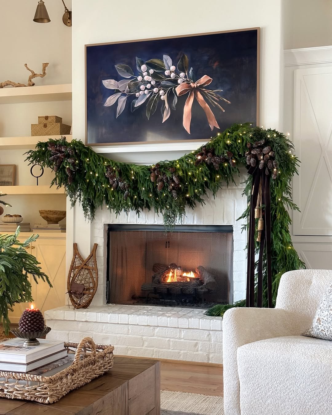 Lush pine and pinecone holiday garland with twinkle lights draped across a white fireplace mantel