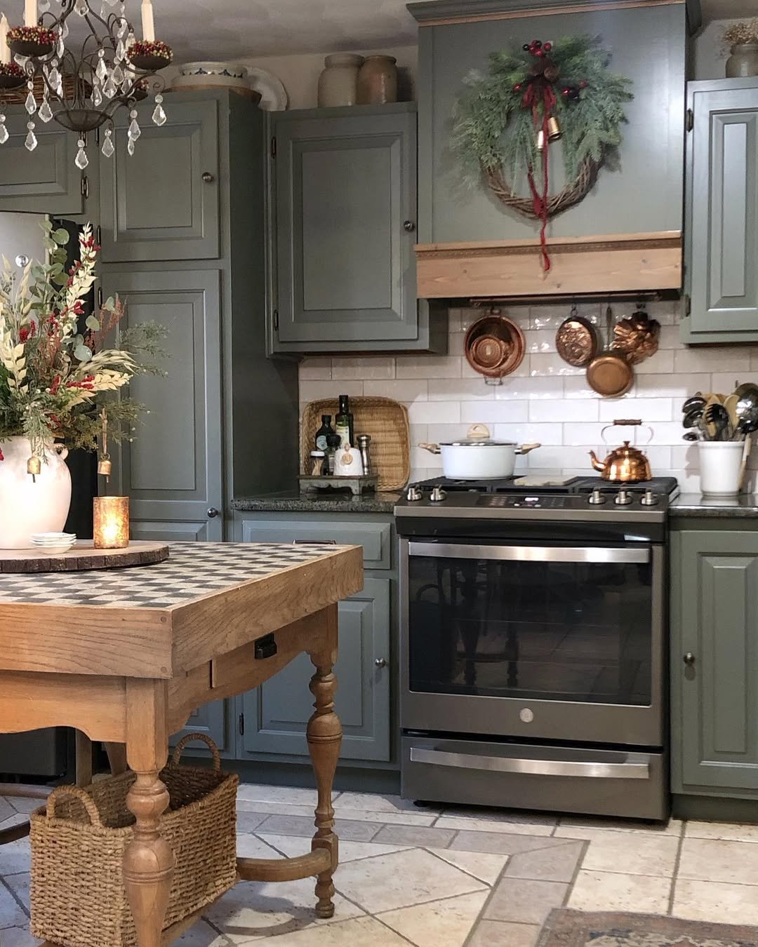 Rustic Christmas kitchen with evergreen wreath, red ribbon, copper pans, and green cabinetry
