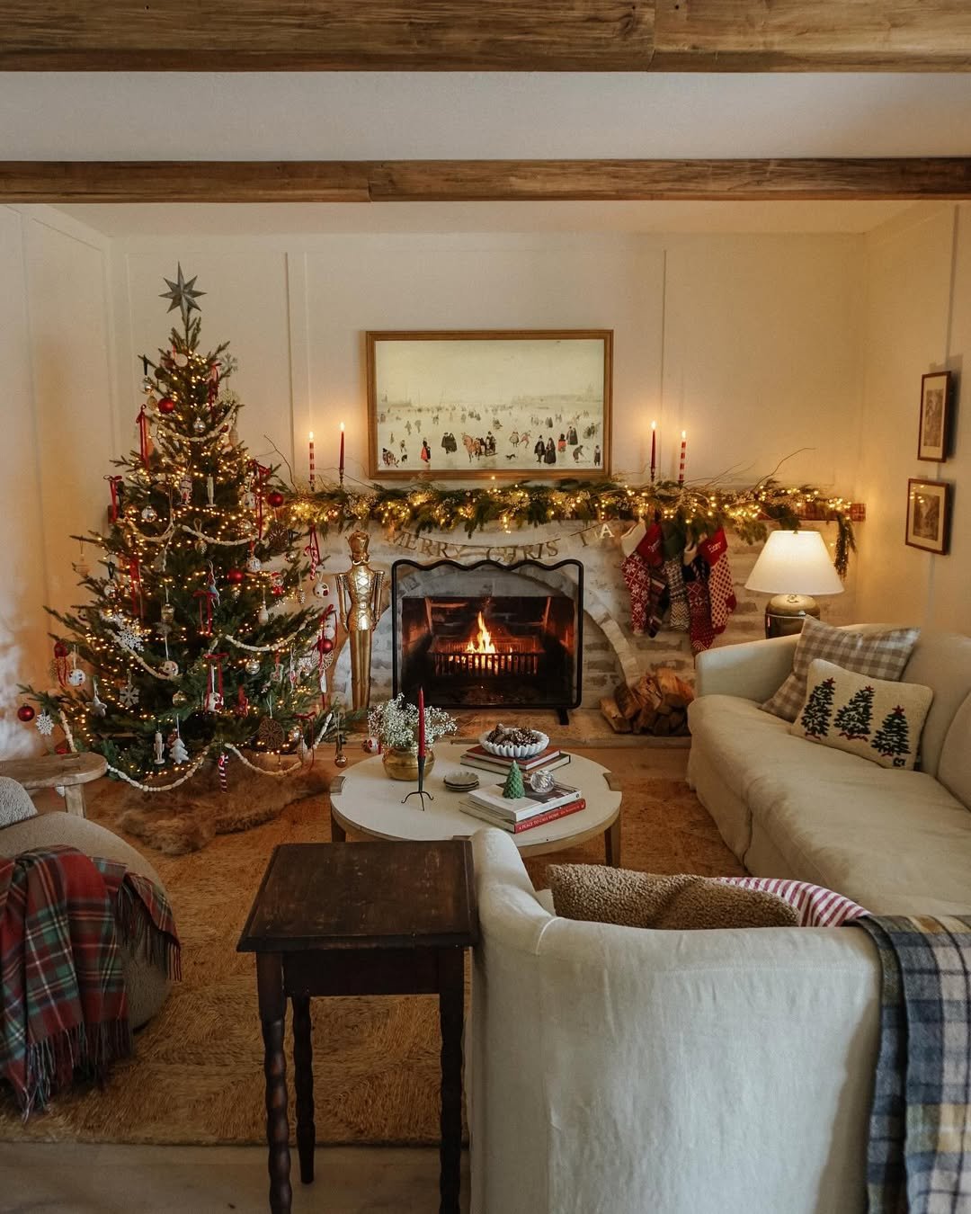Warmly lit Christmas living room with decorated tree, layered mantel garland, stockings, fireplace, and plaid throws