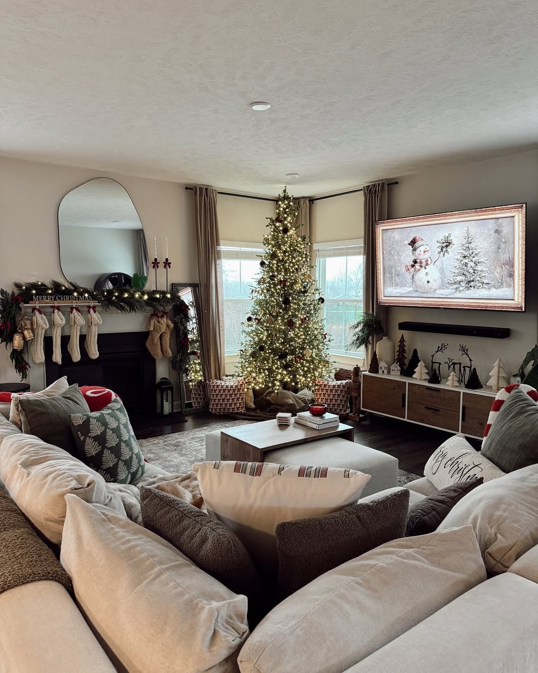 Warmly lit Christmas tree with garland mantel, stockings, neutral seating, and festive winter accents