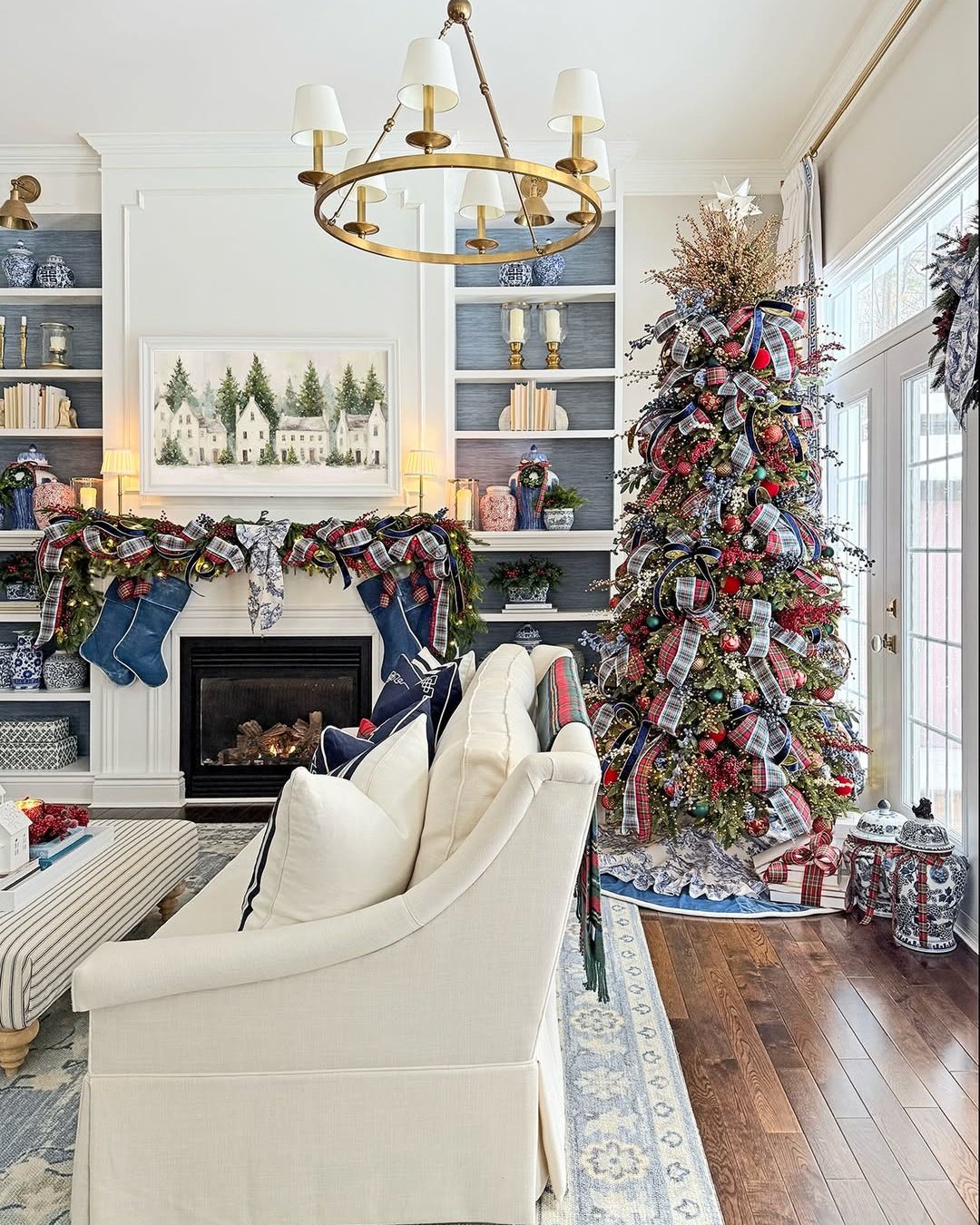 Layered plaid ribbon Christmas tree beside a garland-decorated fireplace in an elegant living room