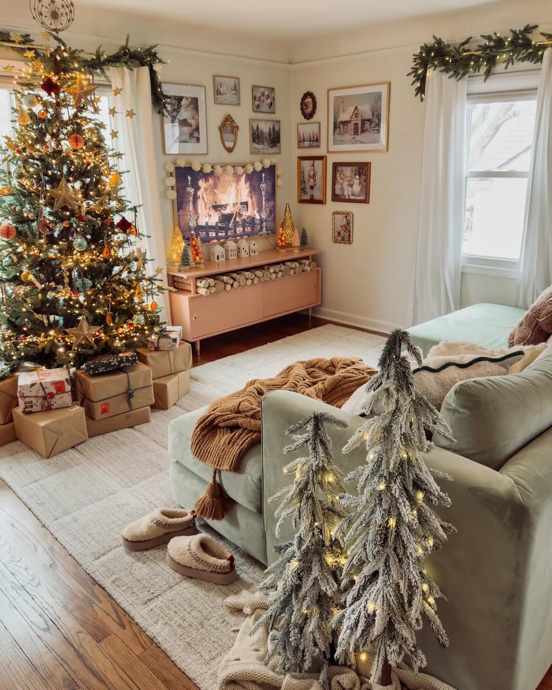 Cozy Christmas living room with glowing tree, frosted tabletop evergreens, garland, wrapped gifts, and vintage artwork