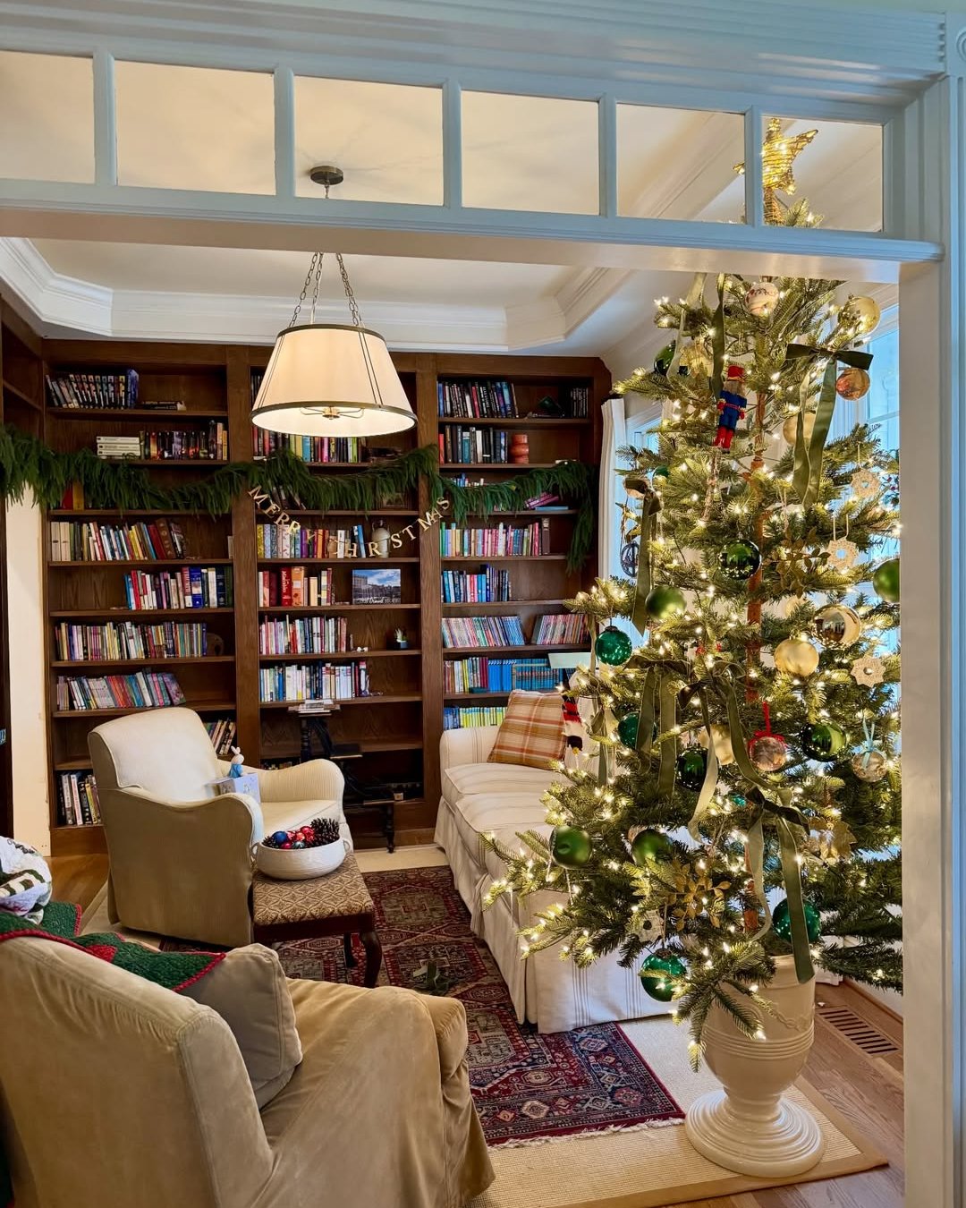 Christmas reading nook with a glowing tree, evergreen bookcase garland, and colorful ornaments