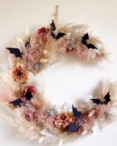 Floral diy halloween wreath with dried grasses, blush blooms, pinecones, and black bat silhouettes