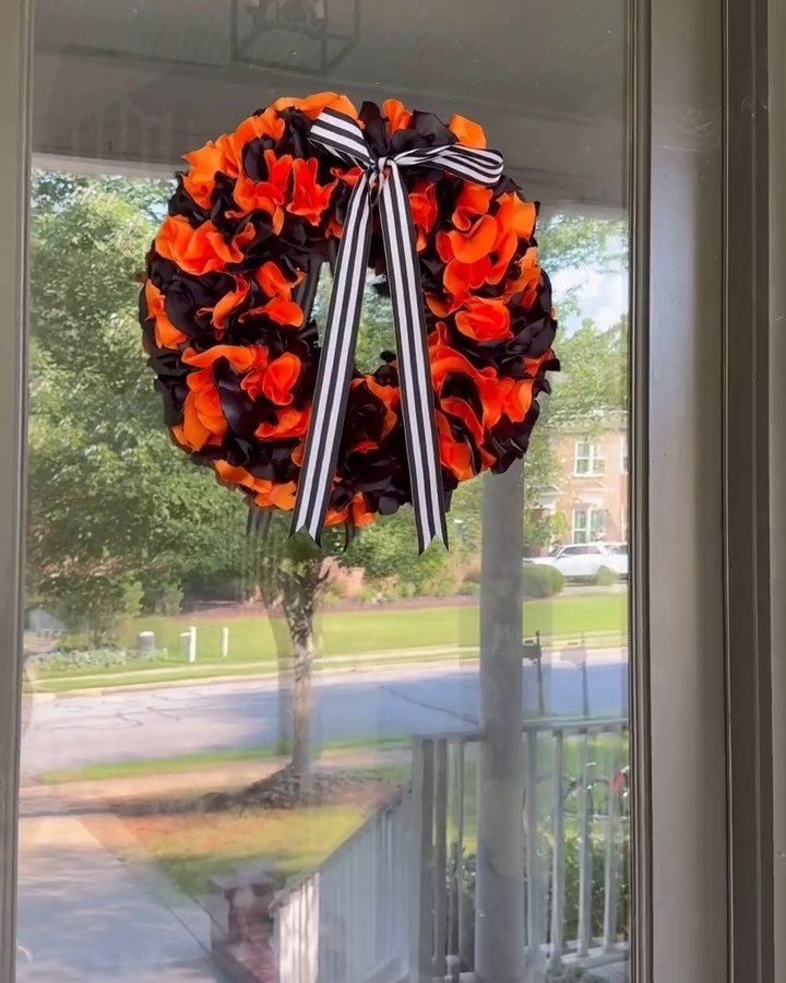 Orange and black fabric wreath with striped ribbon on a glass door